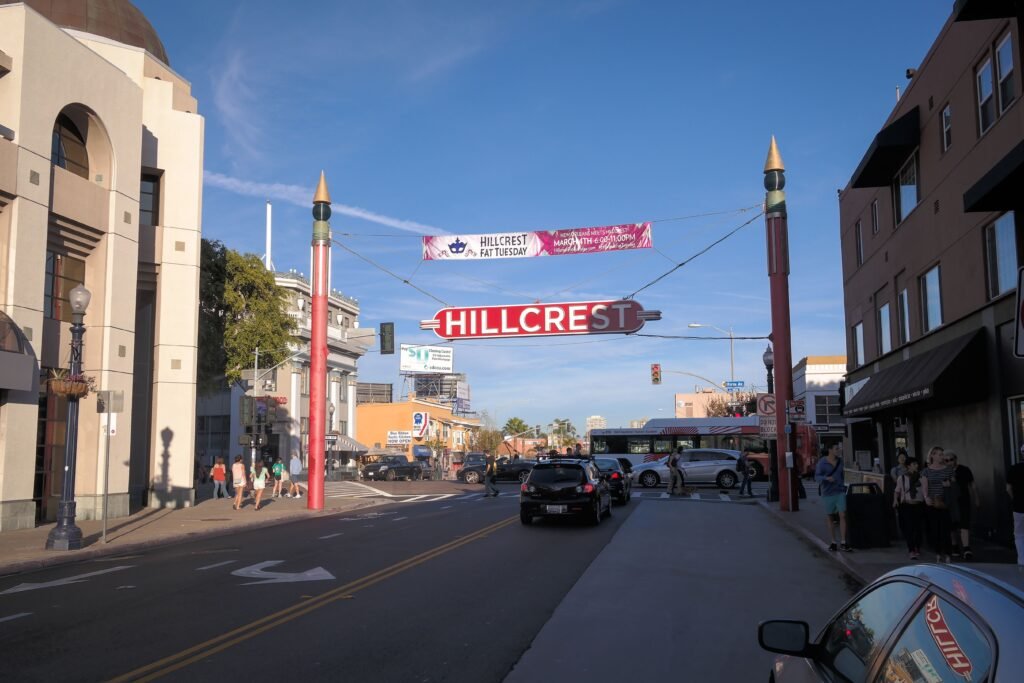 Hillcrest neighborhood entrance sign spanning a busy street with pedestrians, vehicles, and commercial buildings in San Diego.