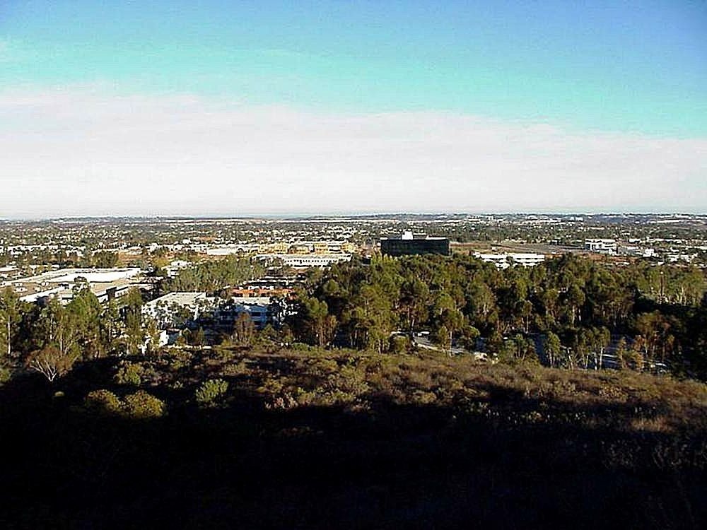 Panoramic view of a suburban business district and wooded hills under a clear blue sky.