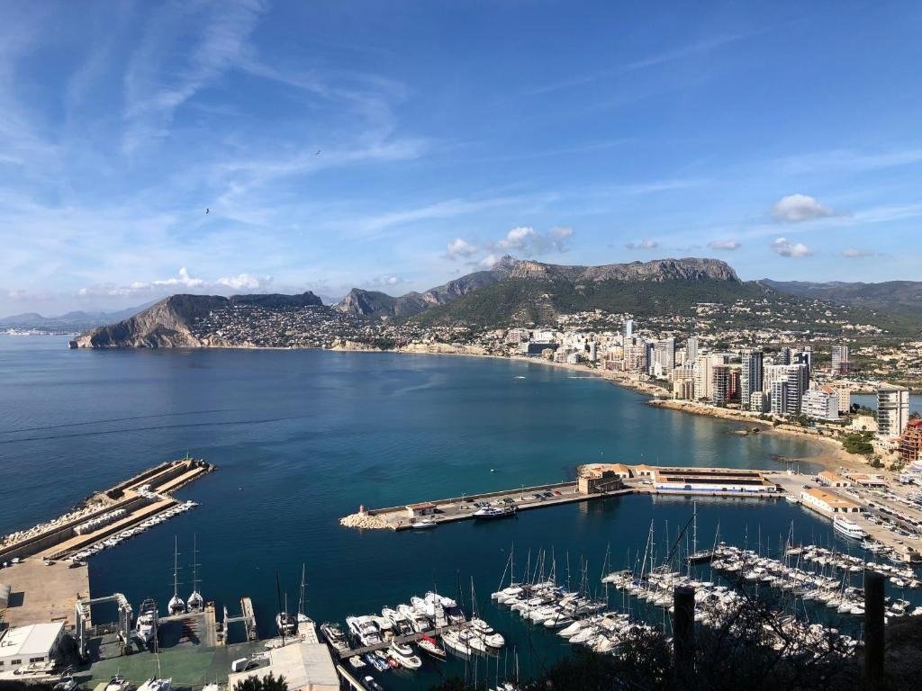 Aerial view of a coastal marina, city skyline, blue bay waters, and surrounding mountains.