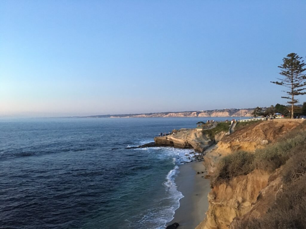 Ocean waves meeting rocky coastal cliffs with scenic shoreline views and a clear blue sky.